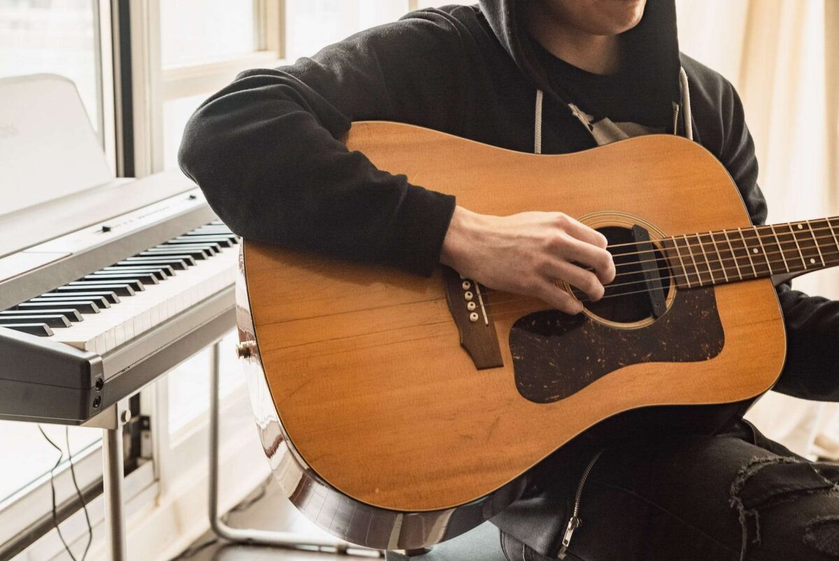 person in black long sleeve shirt playing brown acoustic guitar