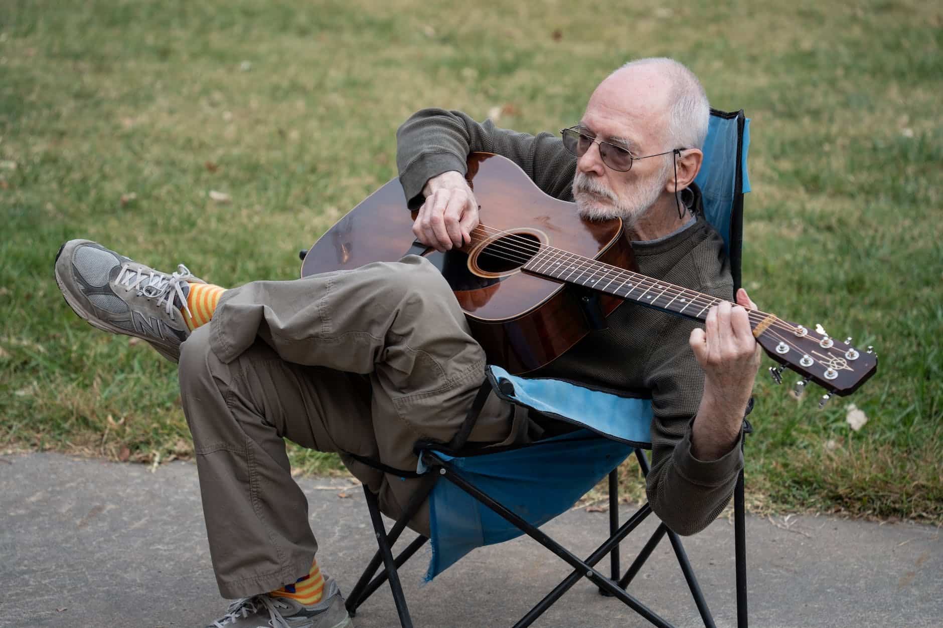 elderly man playing guitar while sitting on camping chair